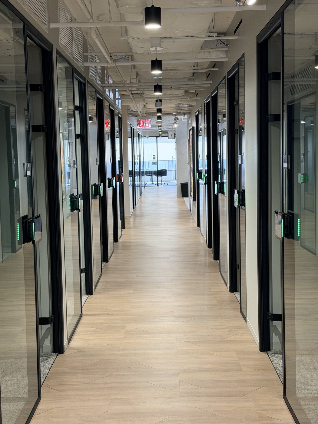 Hallway at Nakupuna's Arlington office lined with glass-walled meeting rooms, the display beside each door showing a green LED status bar