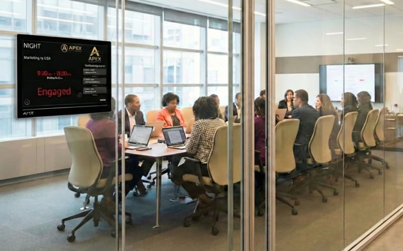 A Door Tablet display mounted beside a glass-walled boardroom, showing the room as engaged